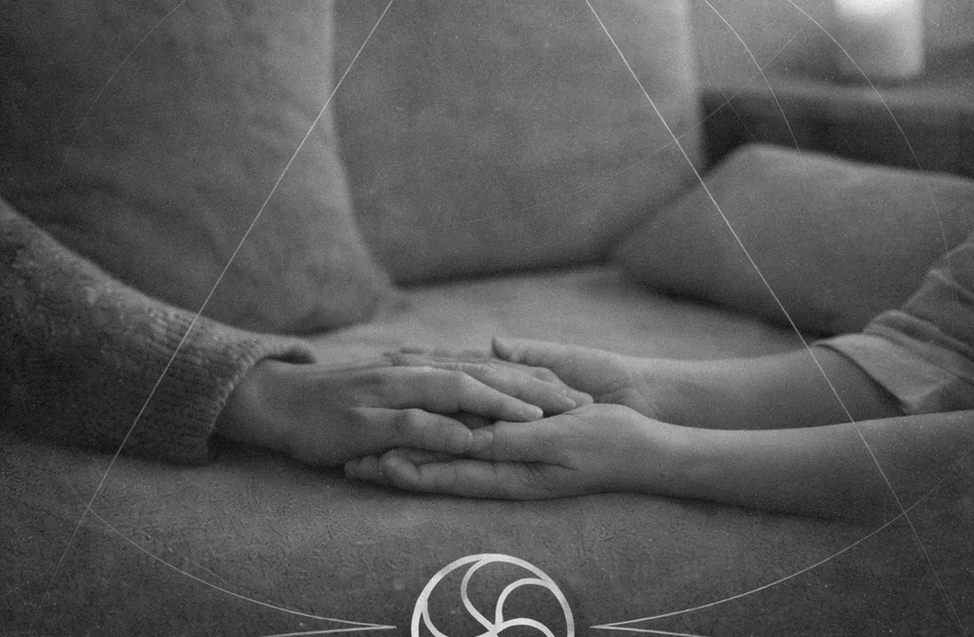 Close-up of a person's clasped hands resting in their lap, in grey tones